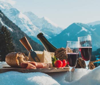wine glasses, plate of susage and chees and bread with snowy mountain background