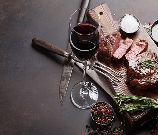 red wine in glass and some meat with a fork and knife